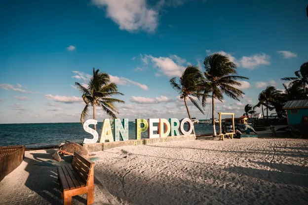 The San Pedro sign on the beach in Ambergris Caye, Belize, with palm trees and white sand at golden hour