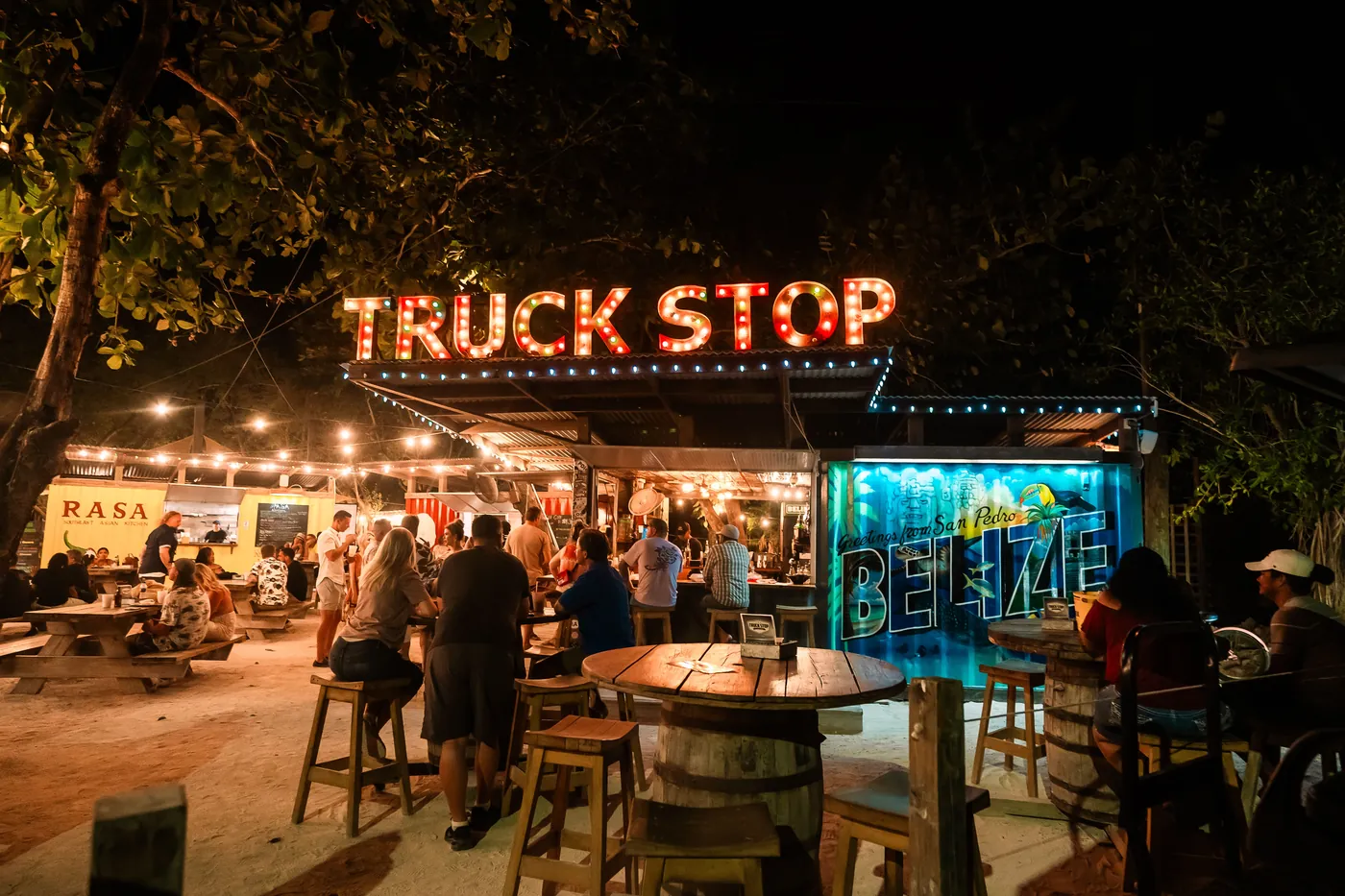 The Truck Stop in San Pedro, Belize at night, a lively open-air food park with string lights and picnic tables